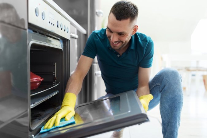 A man with yellow rubber gloves cleans an oven.