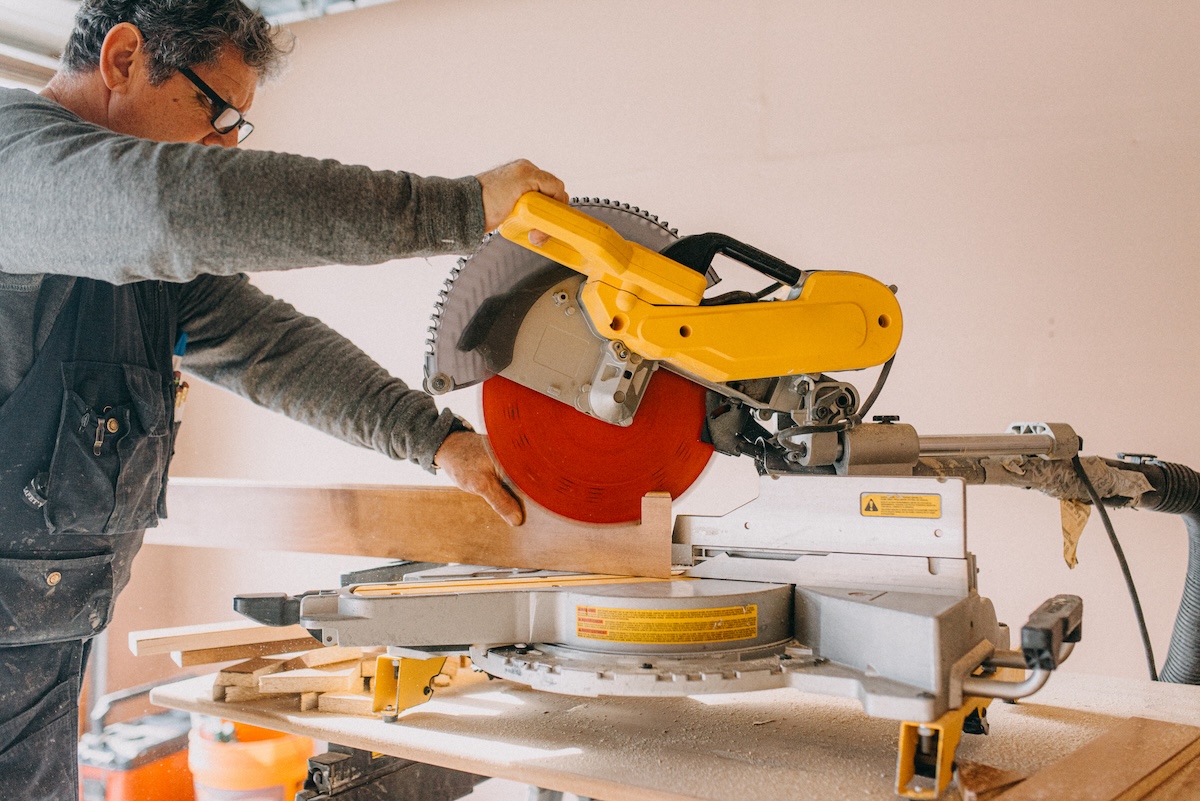 A man uses a miter saw to cut wood in a home renovation space.
