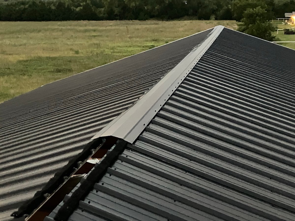 Partially installed ridge venting on a black metal roof.