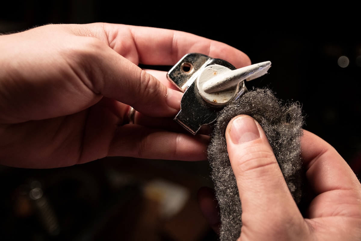 Closeup view of person removing paint or rust from metal door hardware using steel wool.