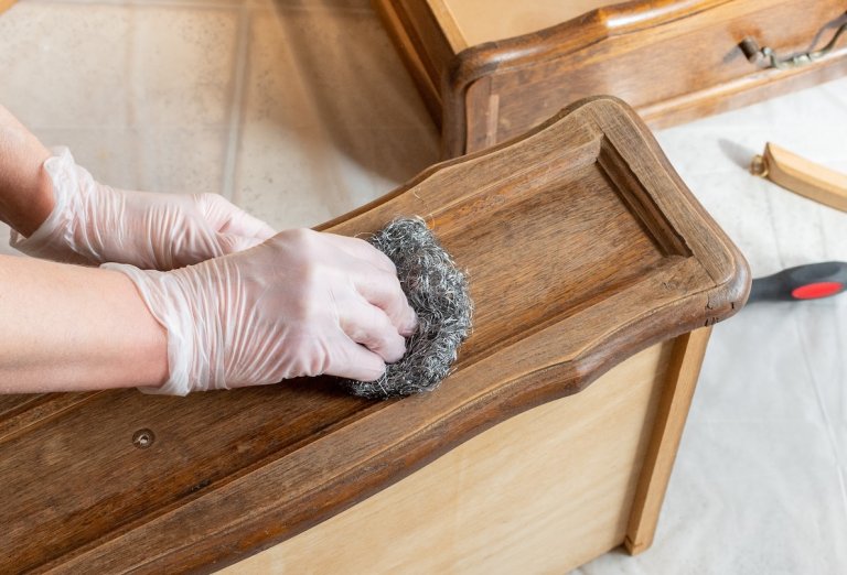 Person wearing nitrile gloves uses steel wool on the front of an antique dresser drawer