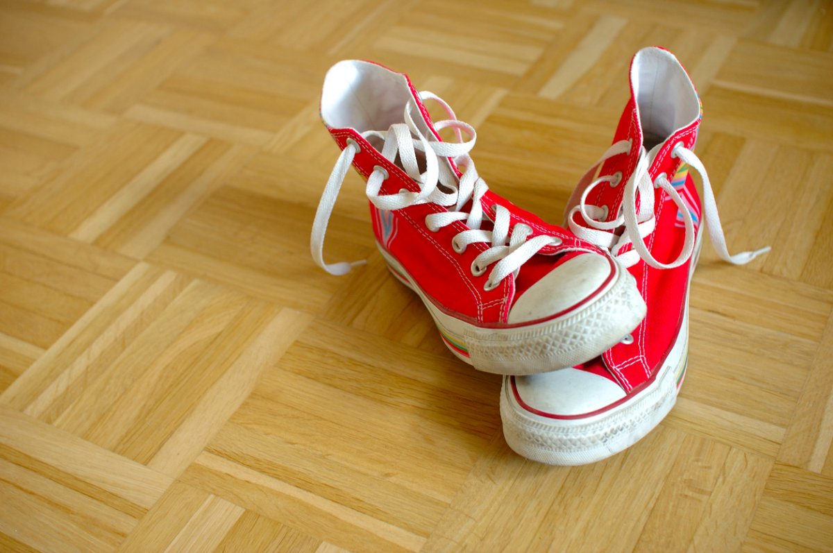 A pair of red Converse high-top sneakers on a Pergo or laminate floor.