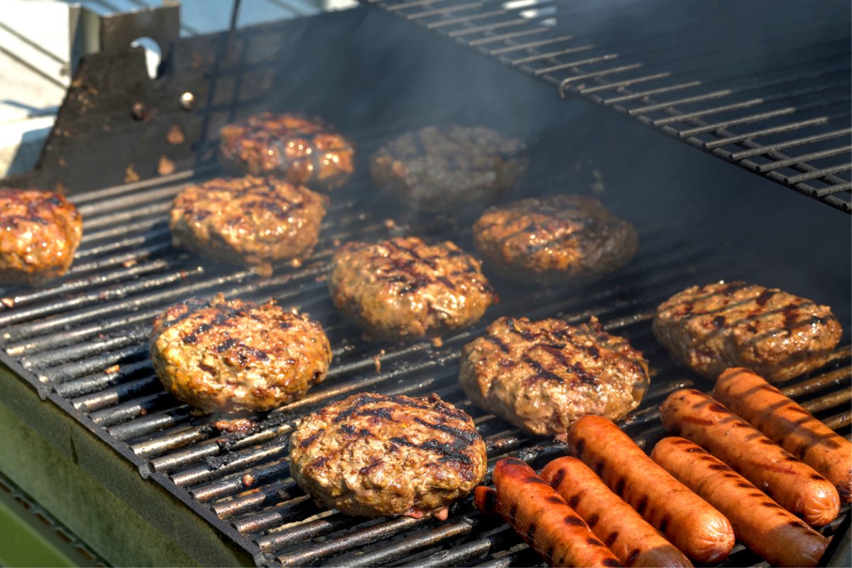 Hamburgers and hot dogs grilling on hot grill grates.