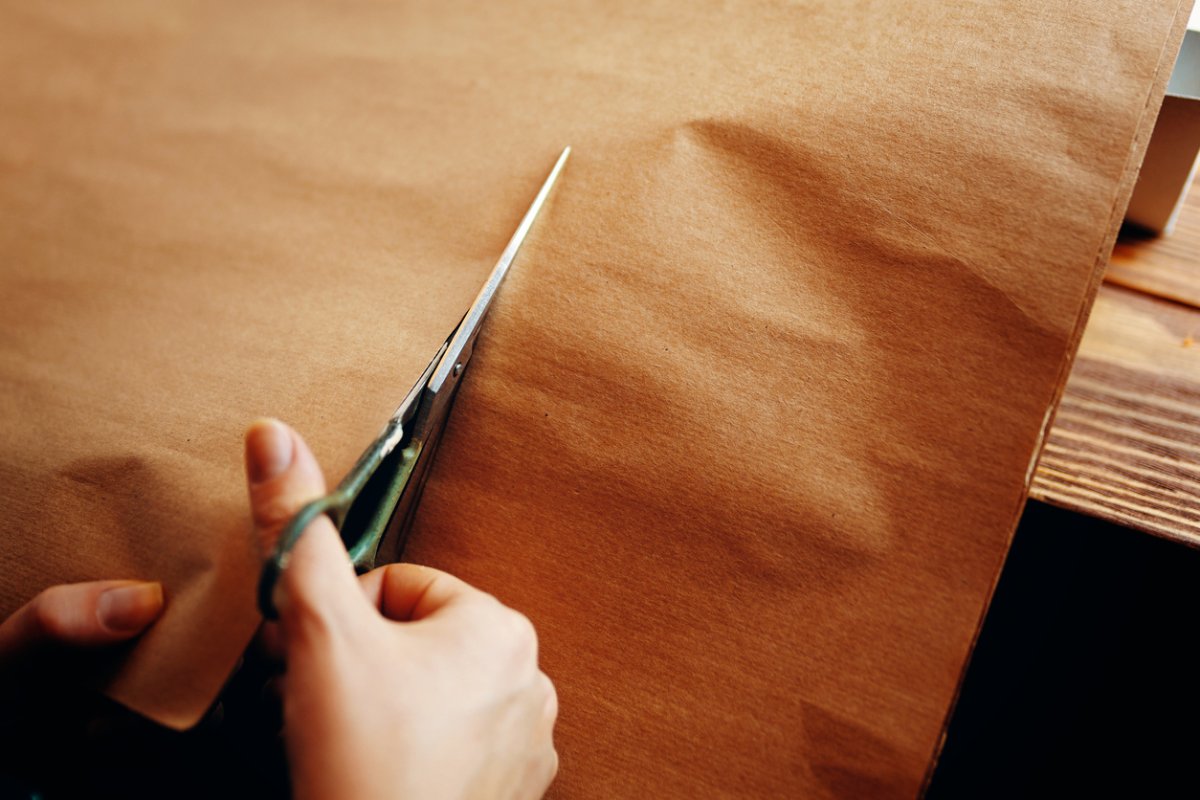 A pair of scissors cutting through brown kraft paper.
