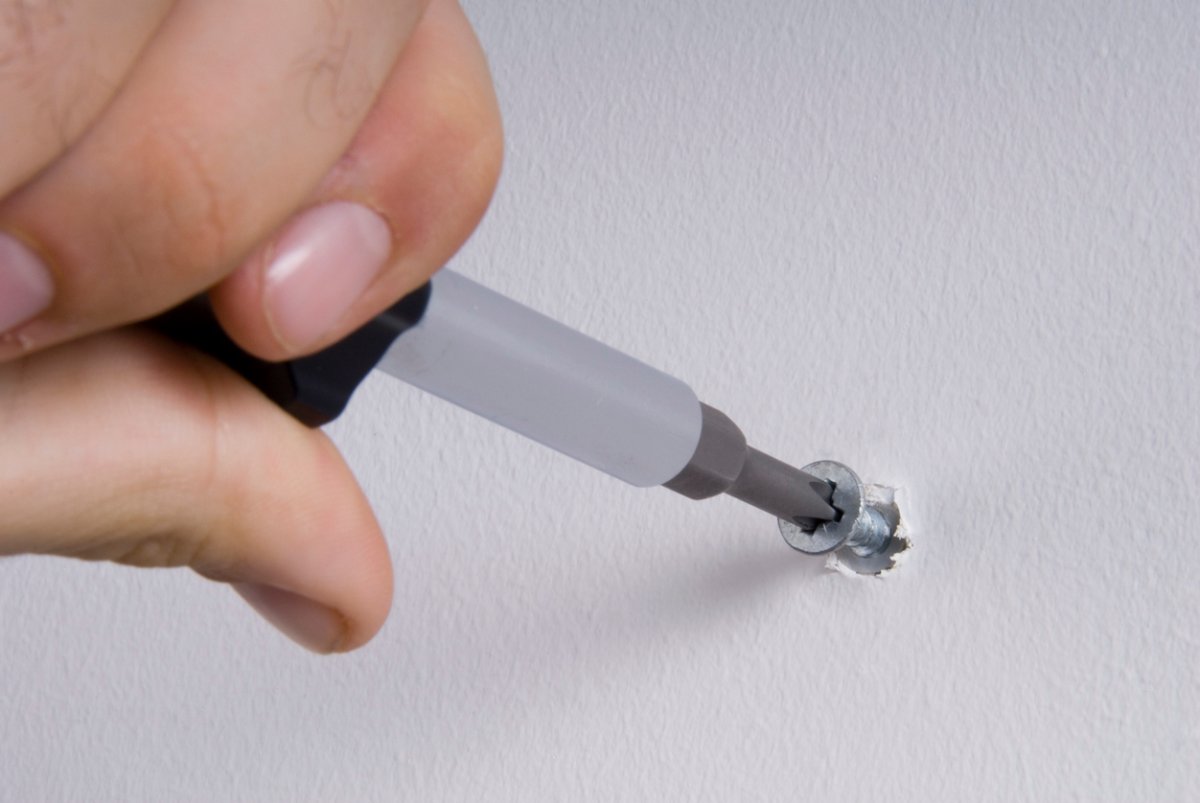 Person's hand uses a screwdriver to tighten a screw in drywall.