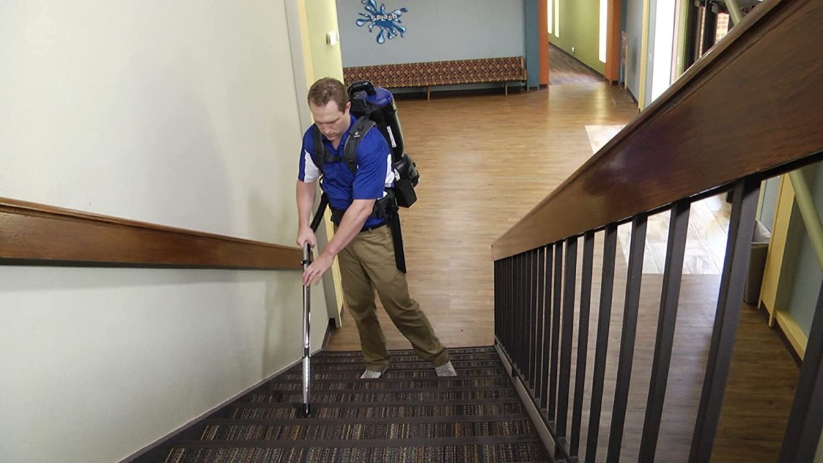 A person using the best backpack vacuum option to clean a carpeted set of stairs