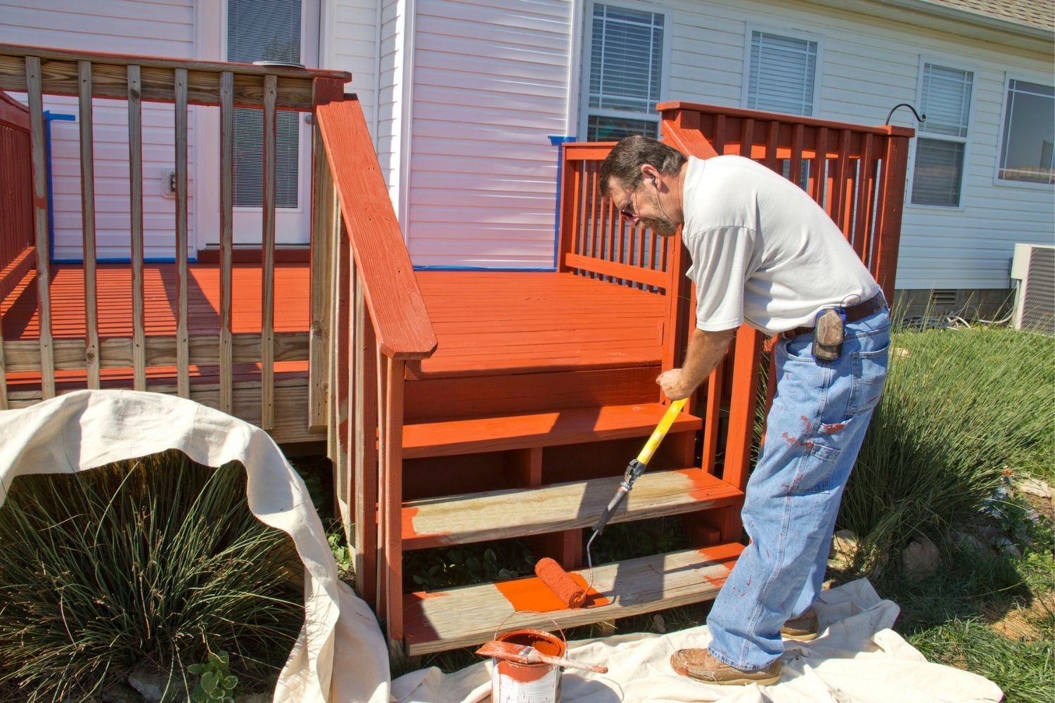 A worker applies paint to a wooden deck using a paint roller.