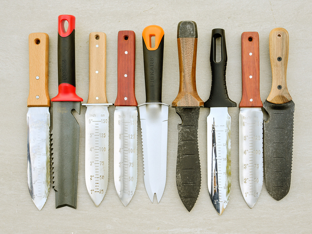A group of all the best hori hori knives laid out next to each other o a cream background.