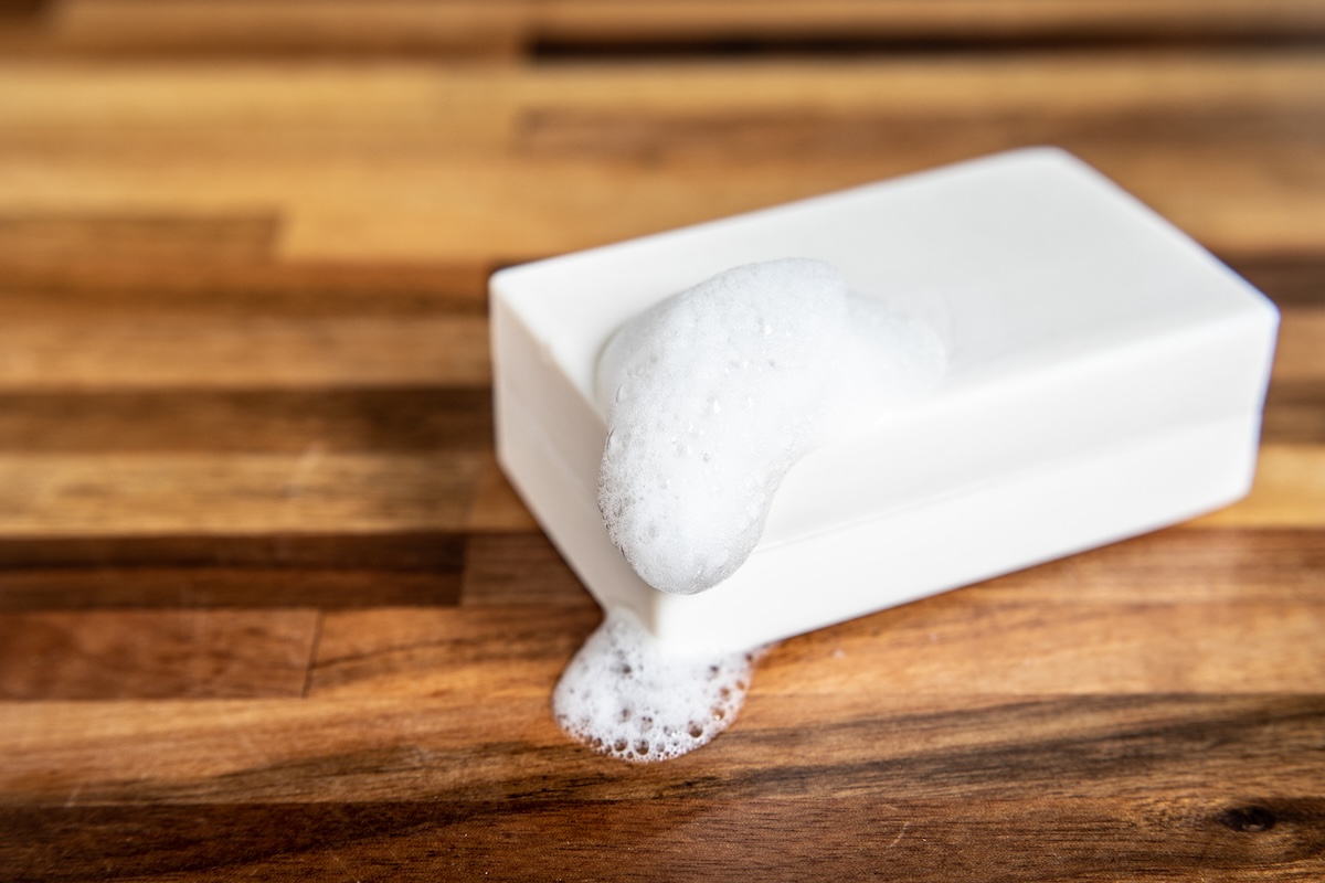 A white bar of soap sitting on a wooden table with bubbles.
