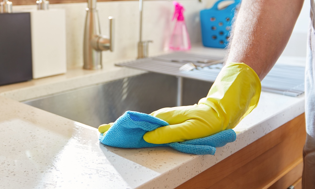 A person with yellow gloves cleans the countertops near an undermount sink.