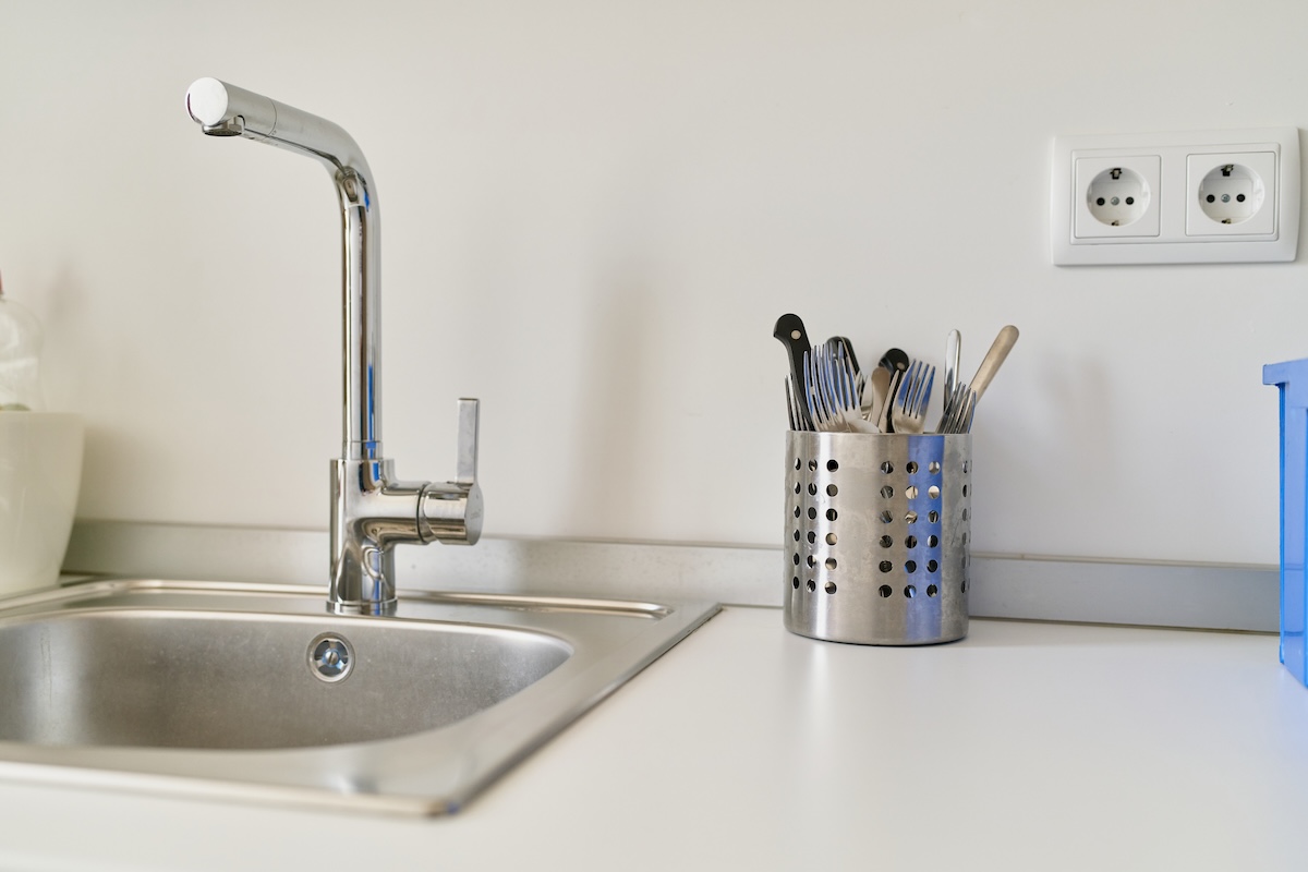 A metal drop in sink surrounded by white countertops.