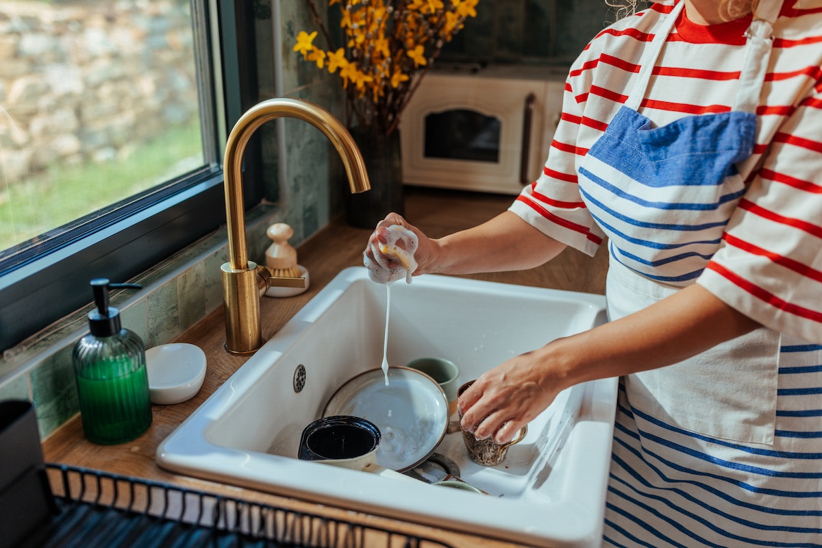 A woman washes dishes in a drop in sink with gold fixtures.