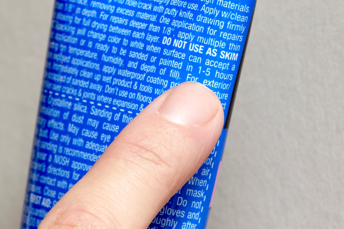 Person points to drying time instructions on the back of a spackle tube.