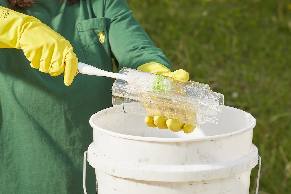 Woman wearing rubber gloves uses bottle brush to clean a bird feeder.