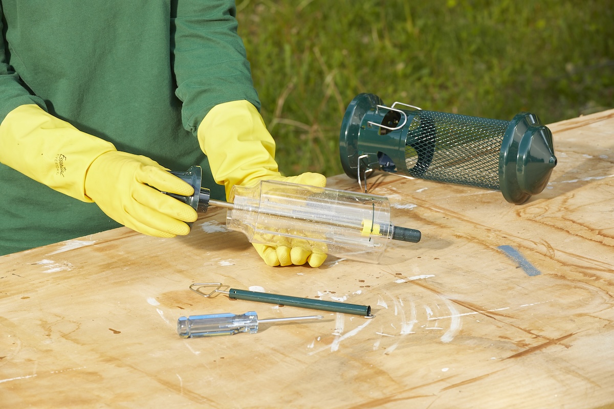 Woman wearing rubber gloves disassembles a seed bird feeder.