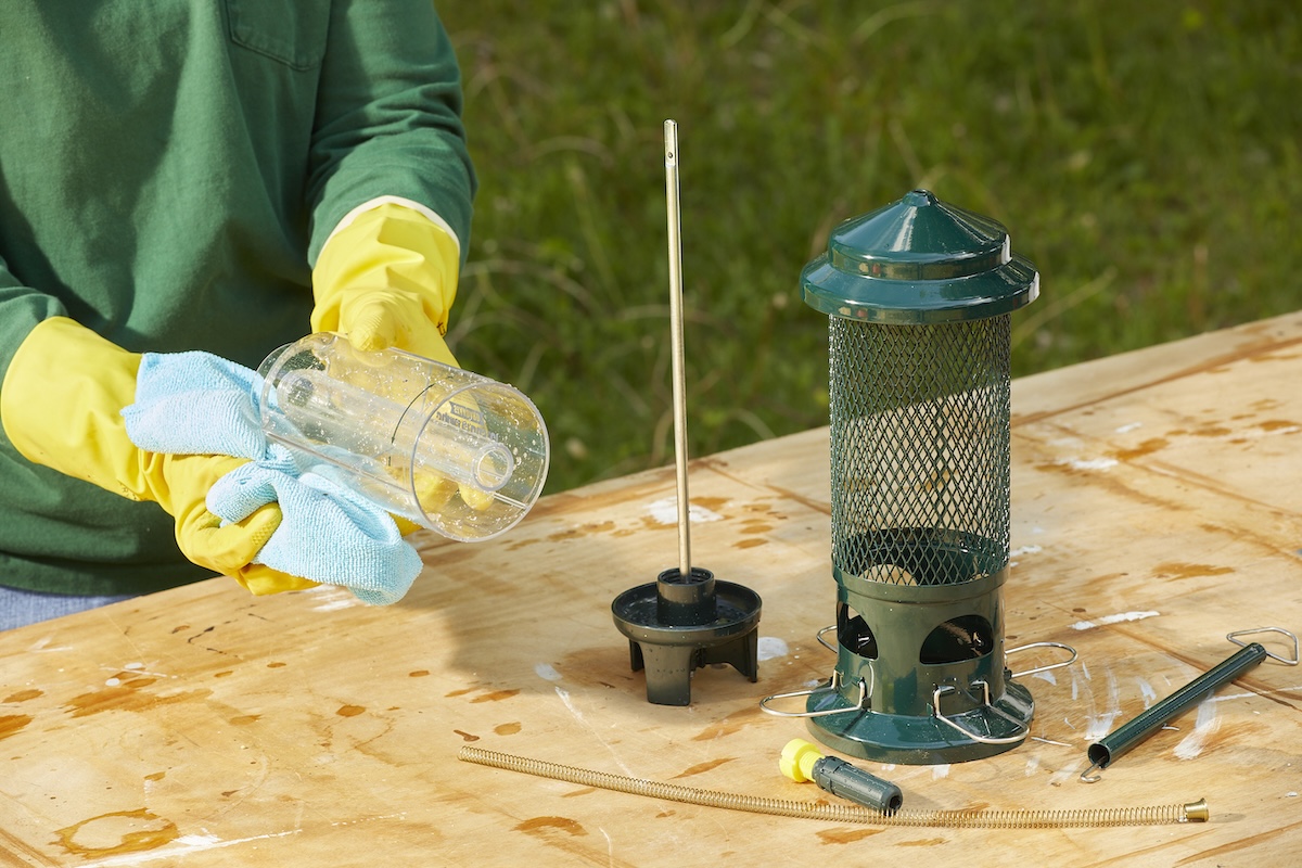 Woman wearing rubber gloves dries parts of a bird feeder with a microfiber cloth.