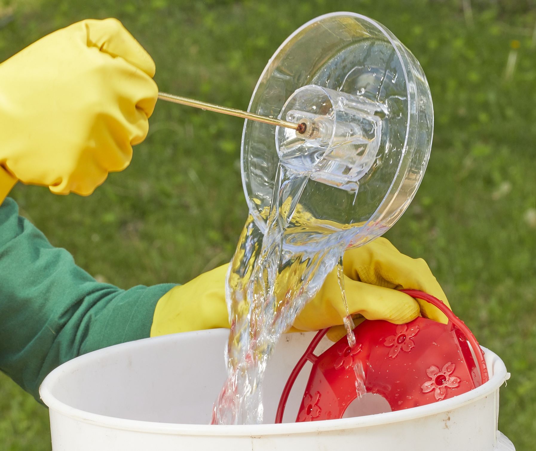 Person wearing rubber gloves dunks hummingbird feeder parts in a large white bucket.