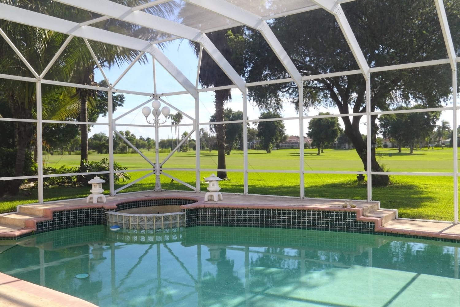 A backyard inground pool and spa combo with a white pool screen enclosure.