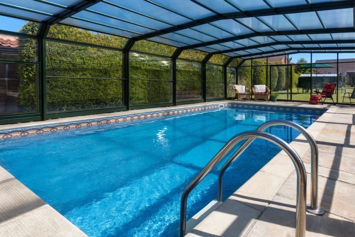 A backyard inground swimming pool with a black-and-glass enclosure protecting it from the elements.