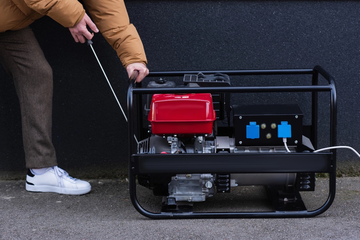 Man wearing white sneakers pulls cord on a portable generator.
