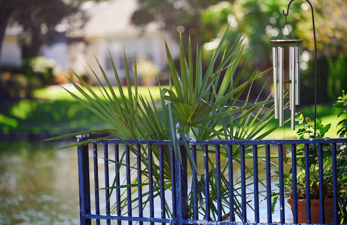 Wind chime hung above a fenced-in garden and flower bed.
