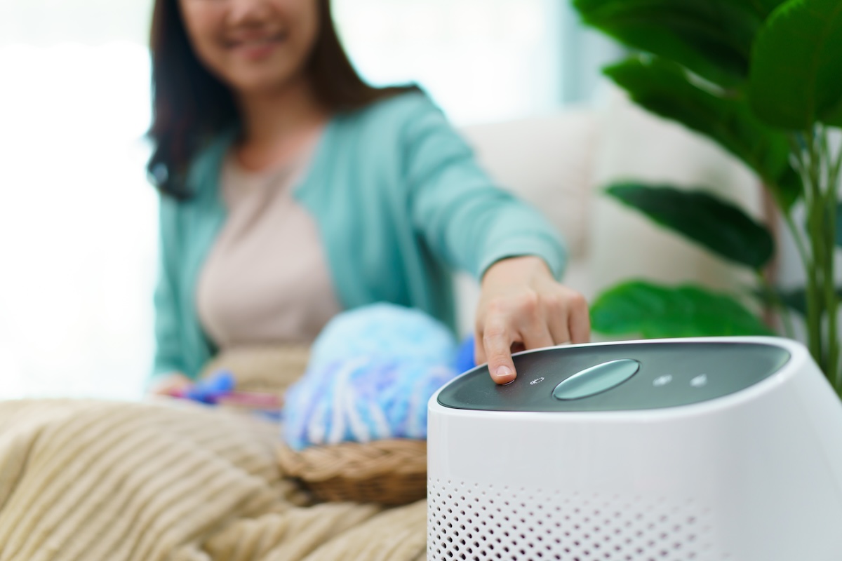Happy young woman turning on high efficiency air purifier while staying and relaxing in the living room.