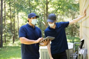 Two contractors dressed in blue go over a details of a siding installation job on a tablet.