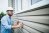 A contractor in a hard hat inspects siding on a house.