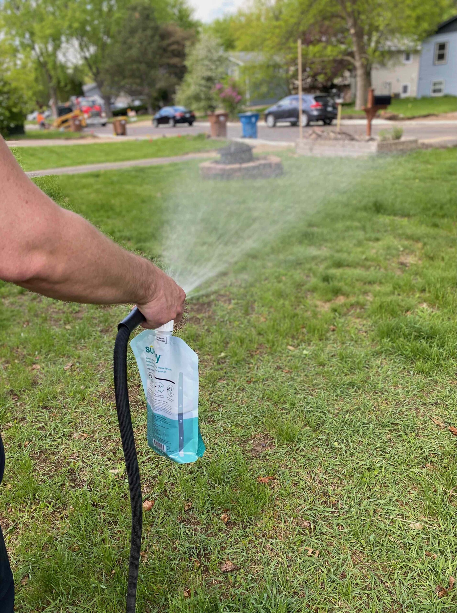 A close up of a person spraying a Sunday lawn care product on a lawn. 