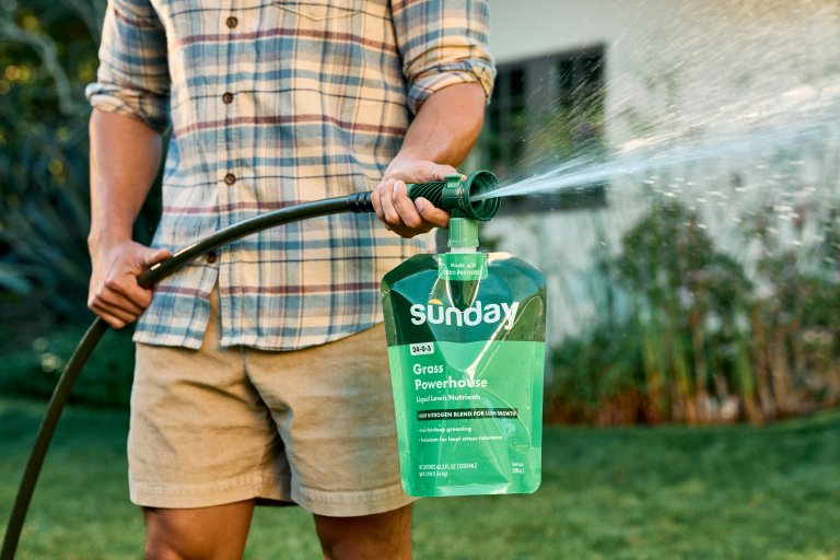 Man spraying Sunday Lawn Care Grass Powerhouse packet to feed the lawn