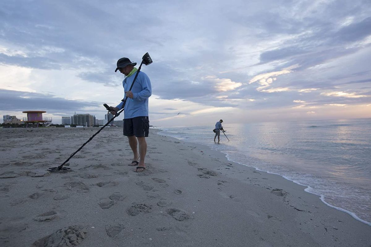 Two people using the best metal detectors for beginners on the beach of an ocean.
