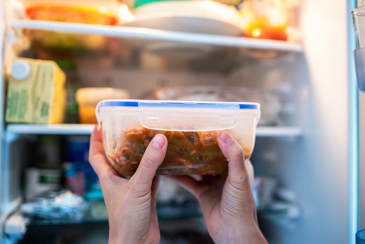 Person holding a food container with a stew in front of a full, open refrigerator.