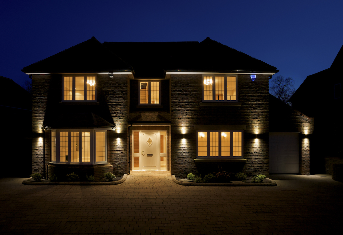 The front and driveway of a luxury home, taken at dusk with all of the interior and exterior lights switched on. 