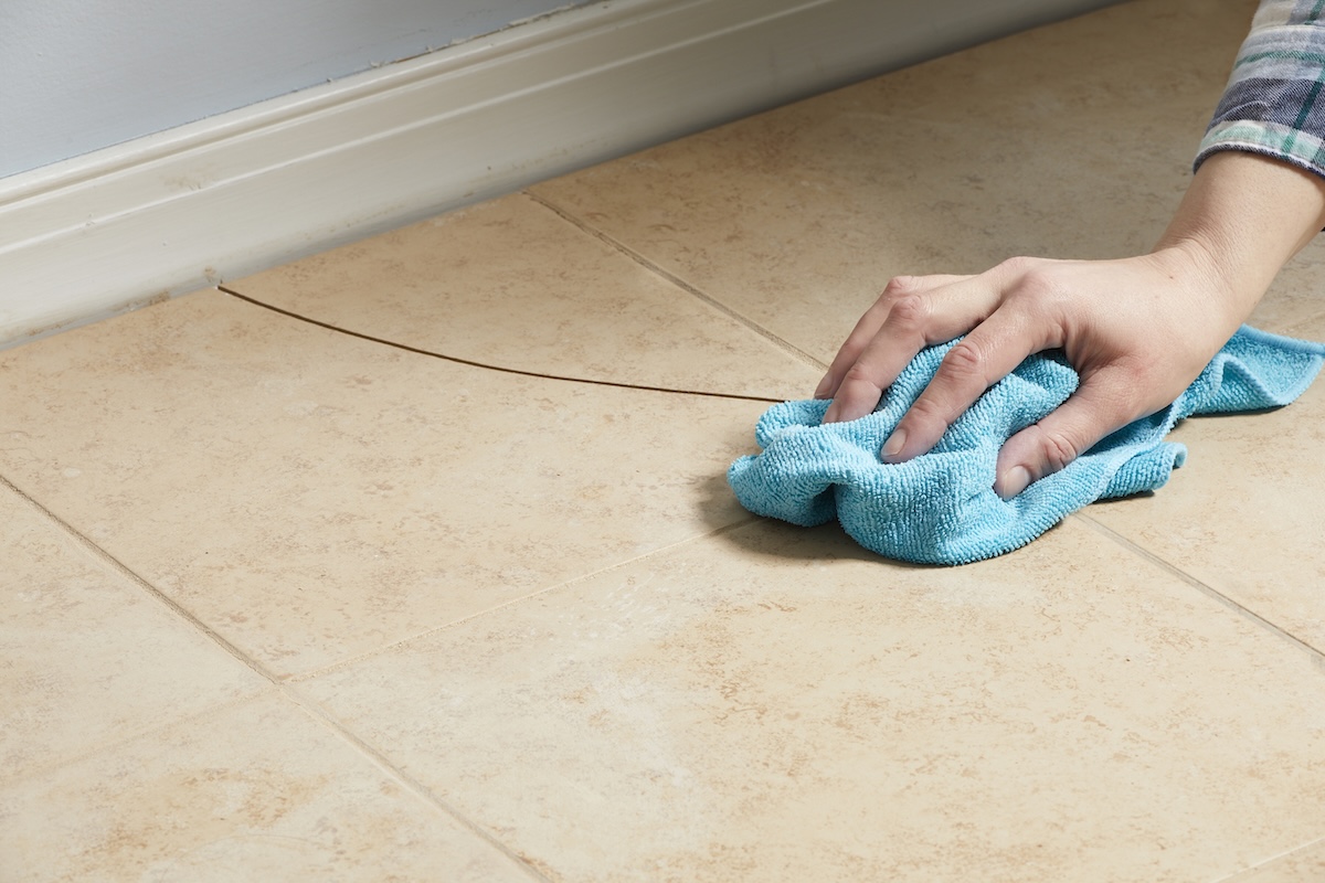 Person cleaning a cracked tile floor with blue microfiber cloth.