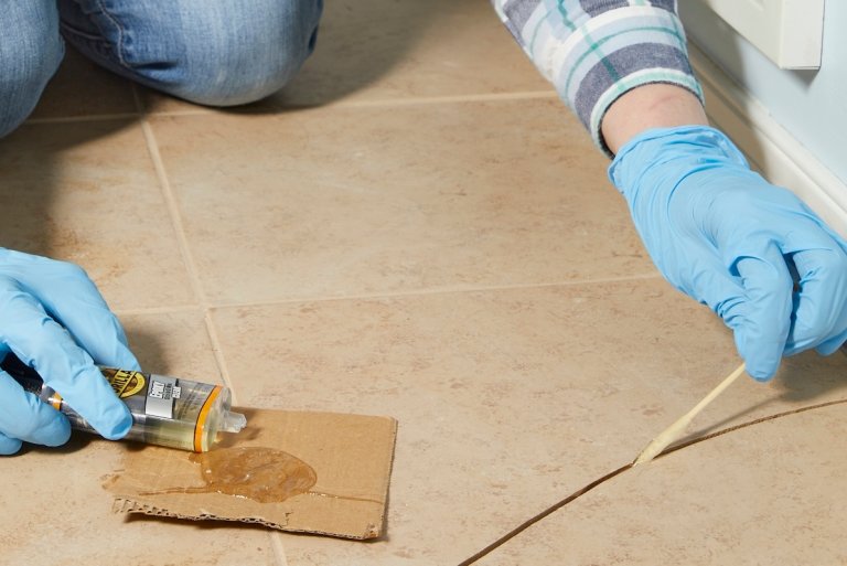 Person uses epoxy to fill a cracked tile in floor.