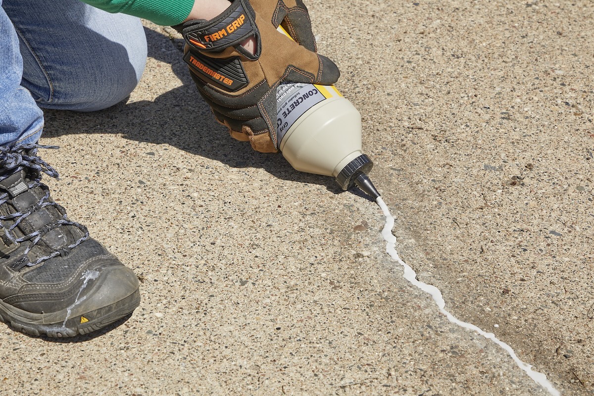 Woman fills crack in concrete driveway with crack filler.