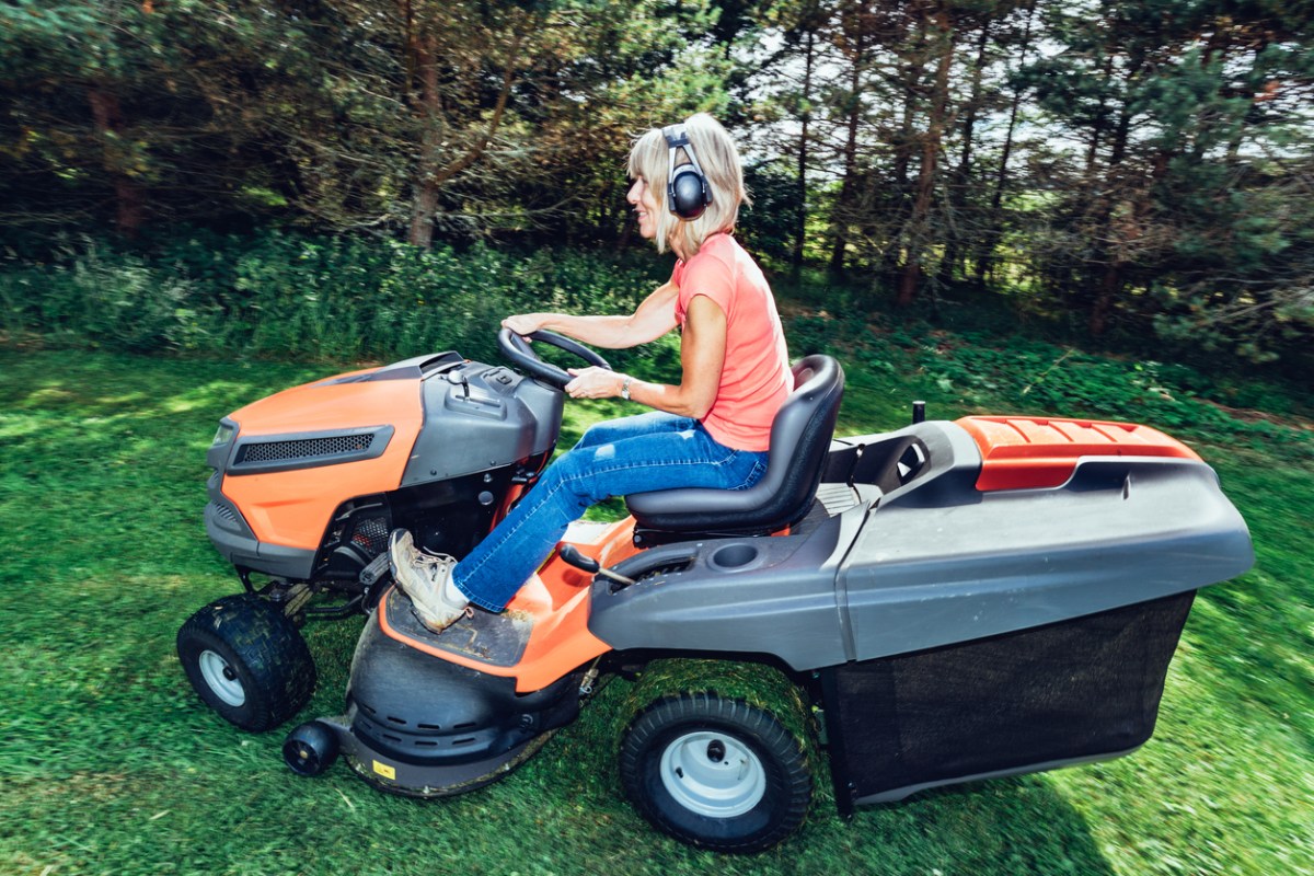 A person using the best ear protection for mowing while using a riding lawn mower in a wooded area.