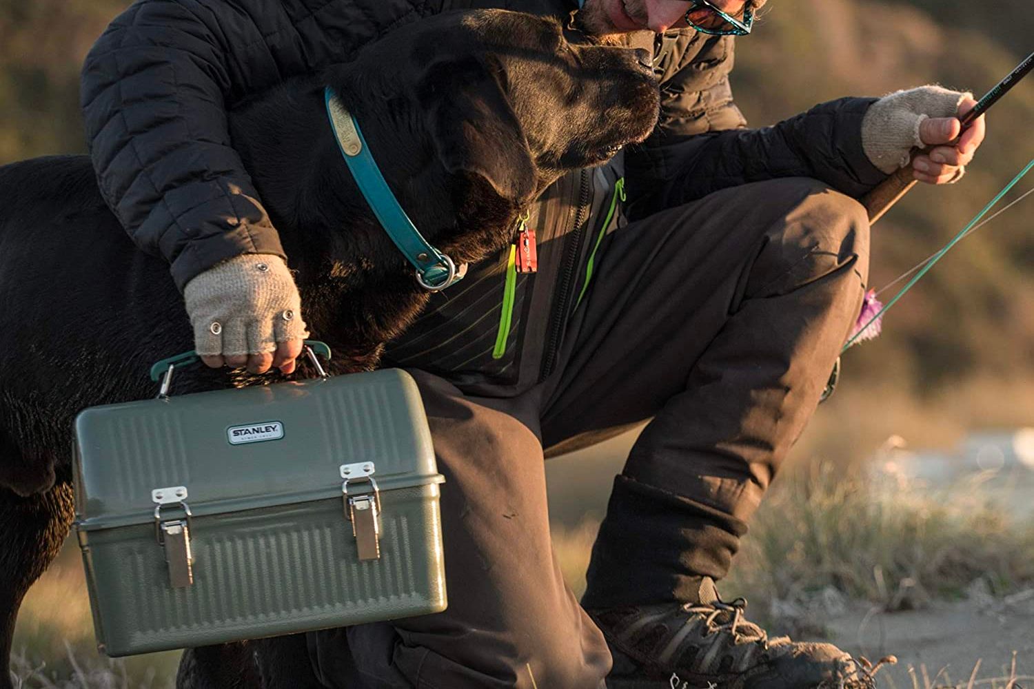 Someone fishing and holding their dark green Stanley lunchbox
