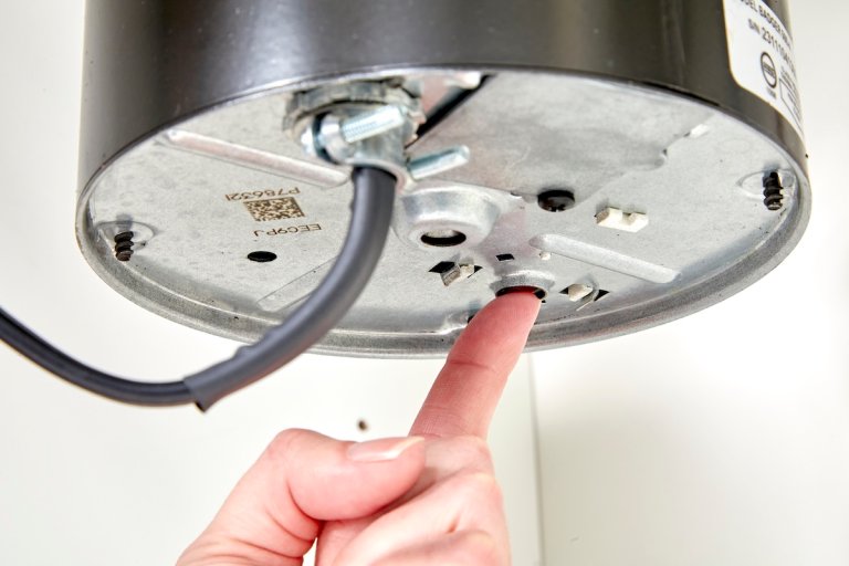 Close up of a person pressing the reset button on the underside of a garbage disposal.