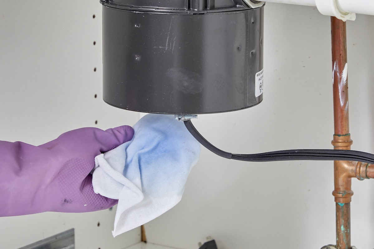 Person wearing rubber glove under under-sink garbage disposal unit catches leaky fluid.