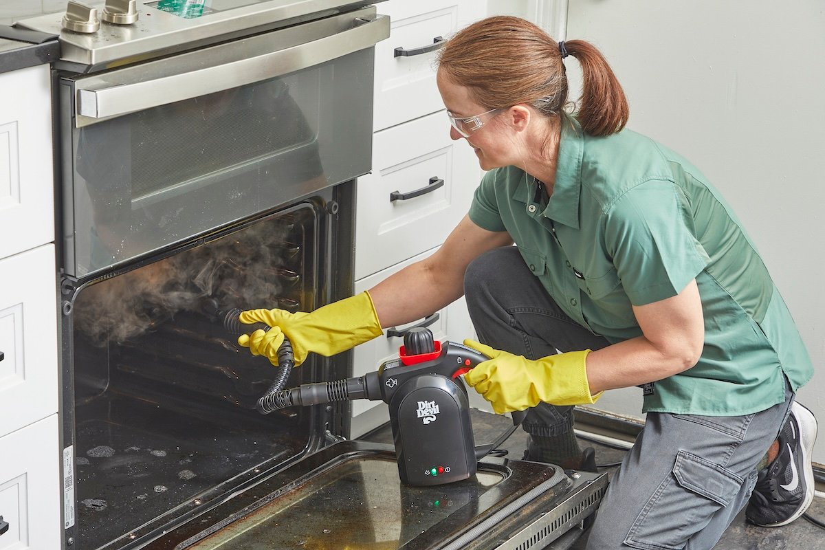 Woman wearing eye protection steam cleans the inside of an oven.