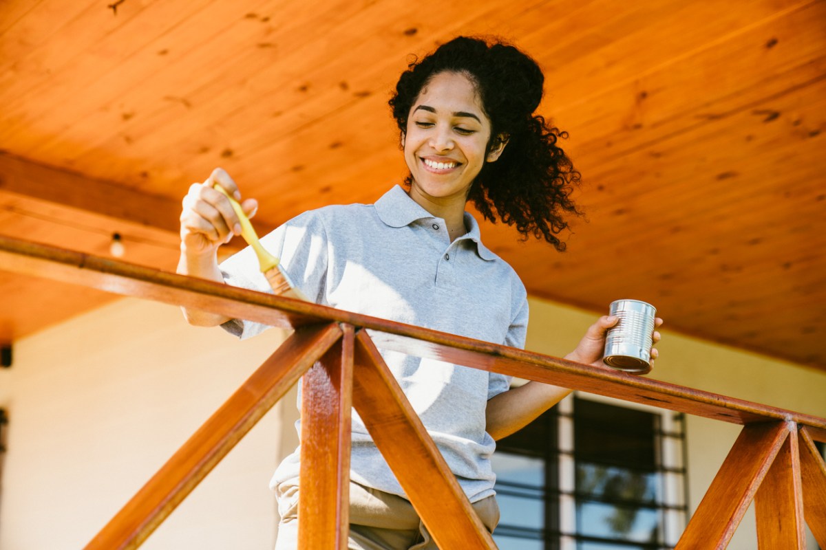 Young woman staining a wood deck railing