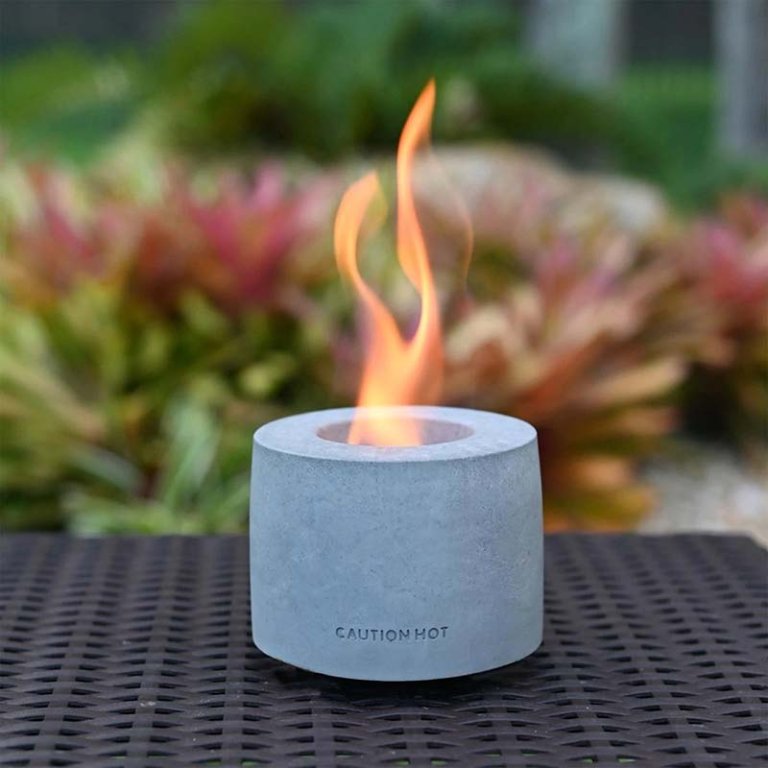  The Colsen Indoor/Outdoor Round Tabletop Fire Pit on an outdoor table with a small flame coming out of it.