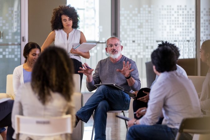A group of people listening to an older man with a beard present at a Home Owners Association meeting.