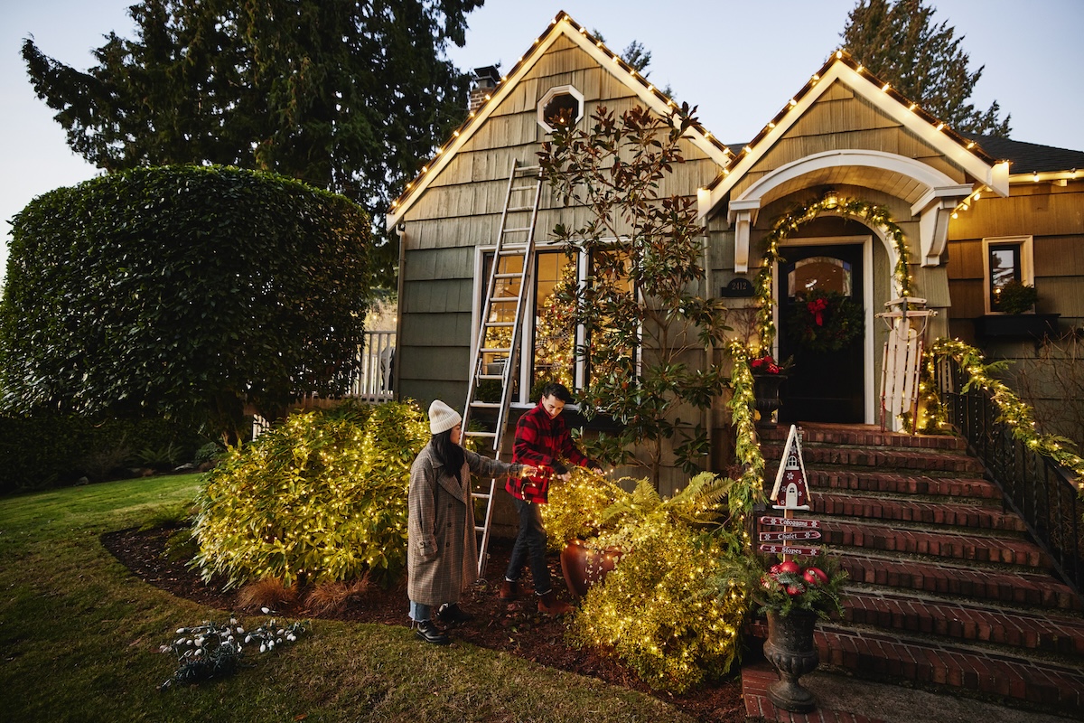 A couple decorating their small bungalow home with Christmas lights.