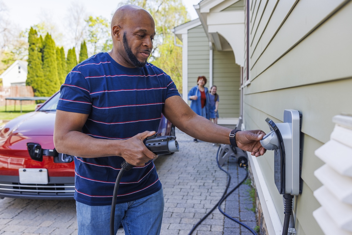 A middle-aged man uses an at-home electric vehicle charger to charge red electric vehicle.