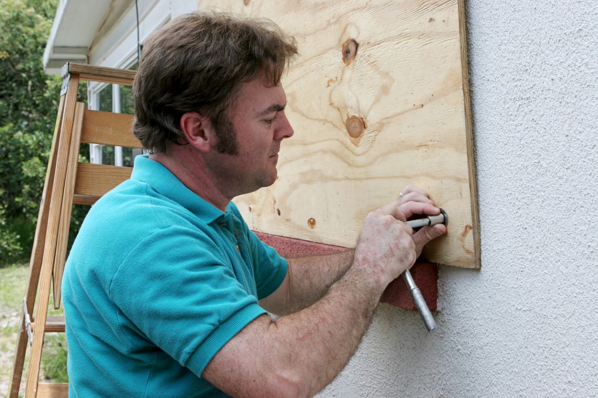 Man wearing a polo shirt attached plywood over a home's window.