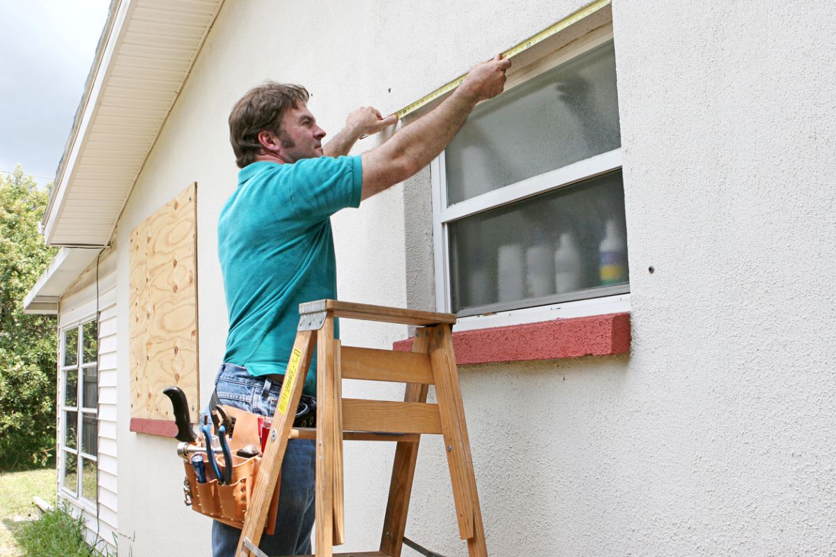 Man stands on step ladder measuring home's exterior window.