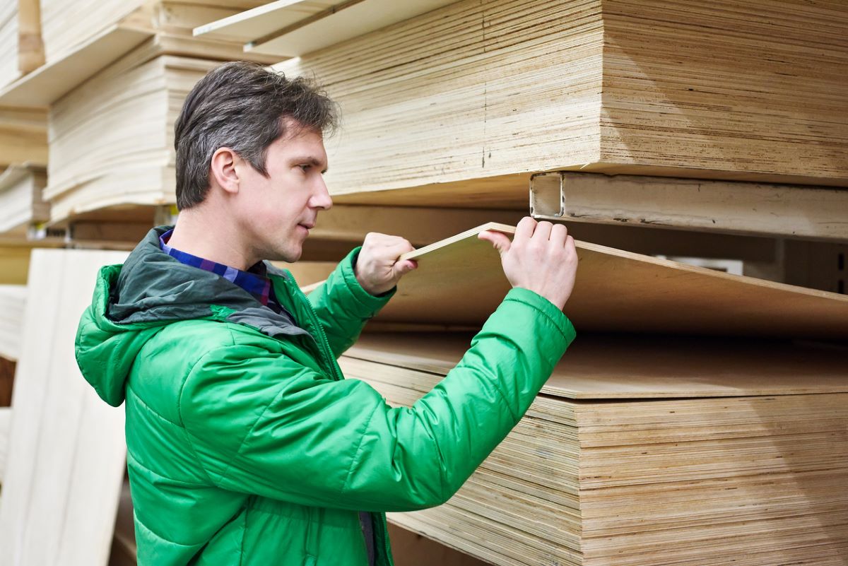 Man in green jacket selects plywood at a lumber store.