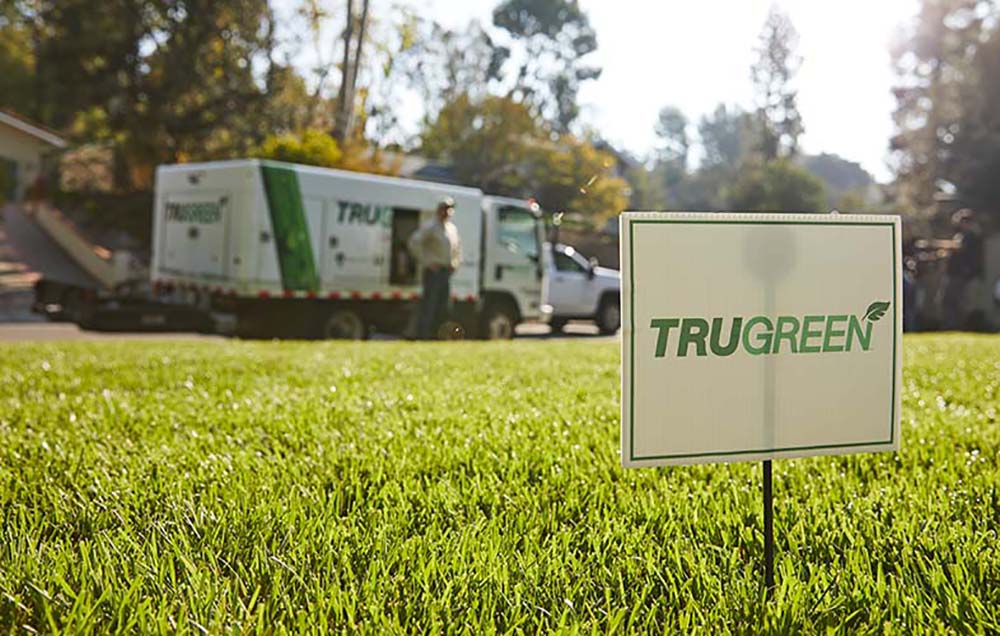 A green lawn with a Trugreen lawn sign in the foreground and a Trugreen company truck in the background.